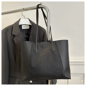 Close-up of black faux leather tote bag with snakeskin texture on a chrome hanger