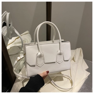 Detail view of a white leather tote bag featuring shield-shaped elements and gold hardware