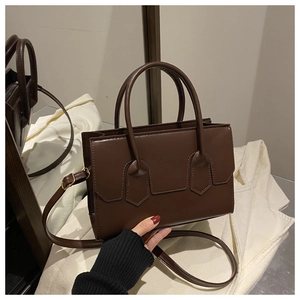 Close-up of a dark brown square crossbody bag with shield stitching and smooth texture