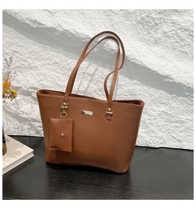 Detail of brown pebbled leather tote bag with silver logo plate and mini envelope pouch