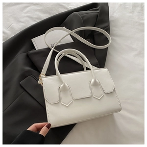 Detail of white PU leather crossbody bag with gold hardware on a black blazer jacket