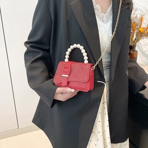 Red crossbody bag with sequined texture flap and pearl handle on a female model