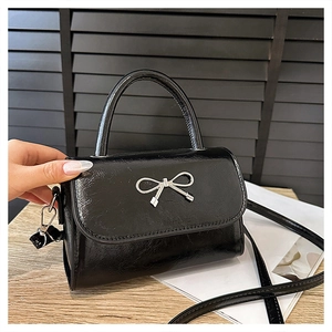 Détail du sac à main en cuir verni noir avec nœud métallique argenté et anse arrondie