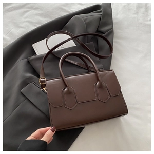 Detail of dark brown faux leather crossbody bag on grey blazer showing smooth texture