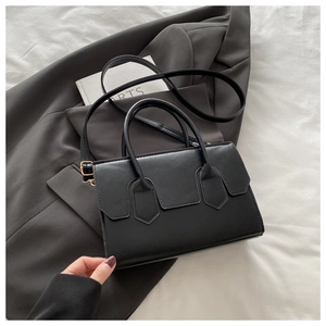 Detail of black leather square bag with gold hardware on minimalist grey blazer