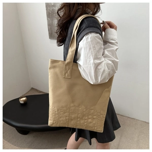 Detailed embroidery texture on the base of a beige canvas tote bag shown on shoulder