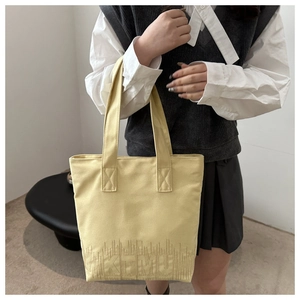Detail of embroidered KTMU lettering on a light yellow canvas tote bag held by a model