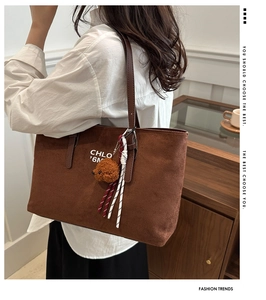 Detail of brown suede tote bag featuring a plush bear pendant and stylish white lettering