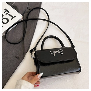 Detail of black patent leather handbag with silver bow metal buckle and arc handle