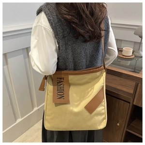 Detail of canvas tote bag with brown trim and fashion patch worn by model at home