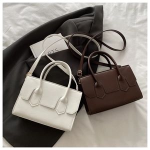 Minimalist white and chocolate brown square shoulder bags on a gray suit and white bedding