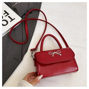 Detail of red patent leather mini bag featuring a silver bow and sleek shoulder strap