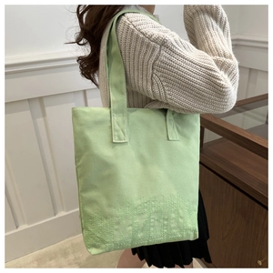 Close-up of mint green canvas tote bag featuring subtle letter embroidery and reinforced straps