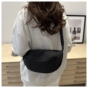 Detail of a black nylon crossbody crescent bag worn on the back over a grey hoodie