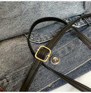 Dettaglio tracolla regolabile in pelle nera con fibbia dorata su sfondo in denim