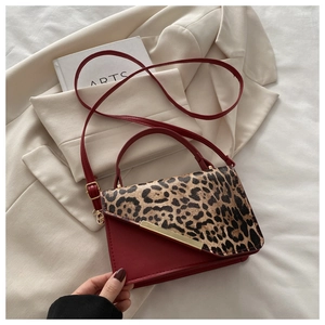 Détail du sac à main rouge et léopard avec garnitures dorées sur un fond doux et neutre