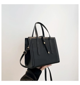 Vertical black tote bag detail with golden metal accents and adjustable strap held by model