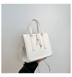 Detailed close-up of white leather tote bag featuring vertical straps and metallic buckle