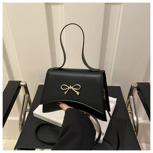 Detail of a black leather handbag featuring a golden bow buckle and unique curved base