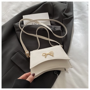 Close-up of cream white handbag featuring a gold metal bow and curved bottom on grey blazer