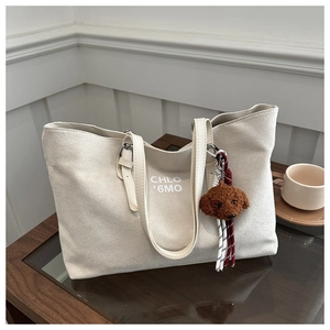 Detail of off-white oversized tote bag with plush dog charm on a wooden table