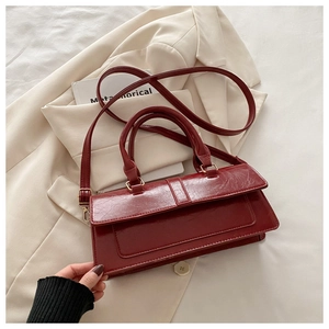 Detail of burgundy patent leather handbag with dual handles and flap closure