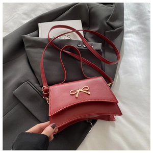 Close-up of a deep red matte leather bag featuring a golden metal bow buckle on a gray blazer