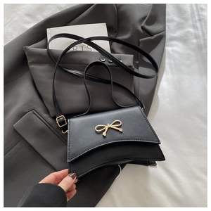 Detail of black crossbody bag with gold bow ornament on matte faux leather finish