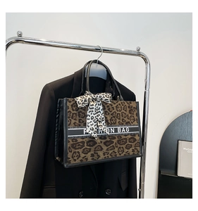 Détail du sac cabas en toile à motif léopard avec nœud décoratif sur une veste noire