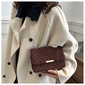 Détail du sac en daim matelassé marron foncé avec bandoulière chaîne sur manteau blanc