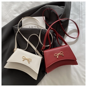 Detail showing white and deep red crossbody bags with golden metal bow buckles