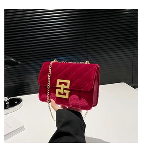 Détail d'un sac à main matelassé en velours rouge avec chaîne dorée et fermoir géométrique