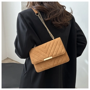 Détail du sac bandoulière en daim fauve avec matelassage en V et chaîne dorée