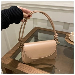 Detailed macro view of the crescent base and knotted strap on this beige underarm bag