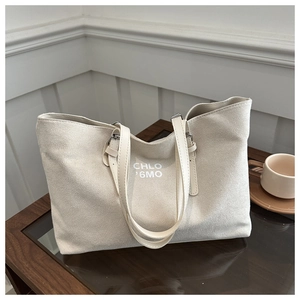 Close-up of beige suede tote bag featuring artistic white lettering on a wooden table