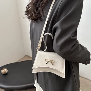 Chic beige crossbody bag with gold bow clasp worn over a grey blazer for spring