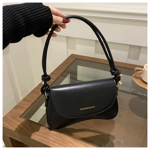 Detail of minimalist black underarm bag with gold logo and cylindrical shoulder strap knots