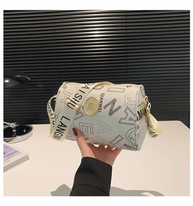 Detail of white cylinder bag with black letter print and gold round metal logo