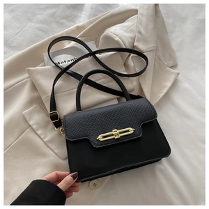 Detail of black textured crossbody bag with gold chain buckle on beige blazer