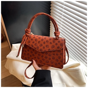 Détail d'un sac bandoulière marron roux avec gaufrage trèfle et poignée nouée élégante