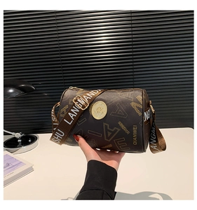 Detail of coffee cylinder bag with letter print, golden logo and wide textile strap