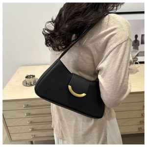 Detail view of black minimalist shoulder bag with gold C-shaped buckle on a model