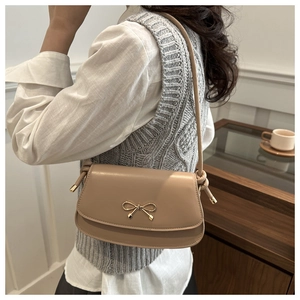 Detail of beige small square crossbody bag with a golden metal bow buckle on curved flap