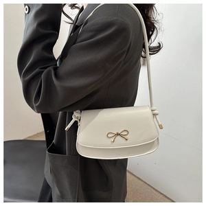 Detail of elegant cream white crossbody bag with a decorative gold bow metal clasp