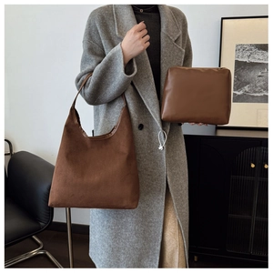 Brown suede tote bag and leather pouch shown with a grey coat in an elegant home setting