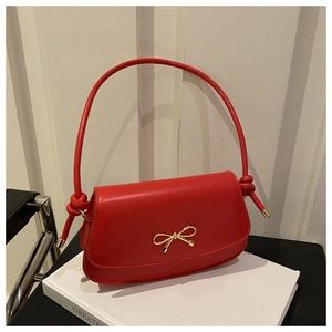 Detail of red crossbody bag featuring gold bow lock and creative knot strap accents