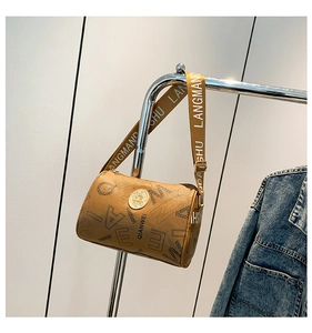 Detail of a brown cylinder bag with letter prints and a golden circular logo