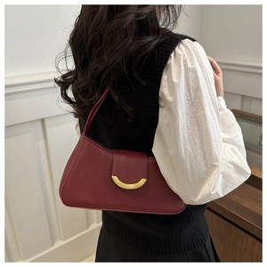 Close-up of a burgundy shoulder bag with a crescent gold buckle on a model in black and white