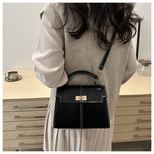 Détail d'un sac bandoulière noir avec coutures blanches et fermoir rotatif doré