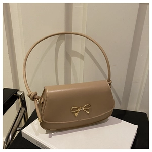 Close-up of beige faux leather bag featuring a gold bow clasp and knotted strap detail